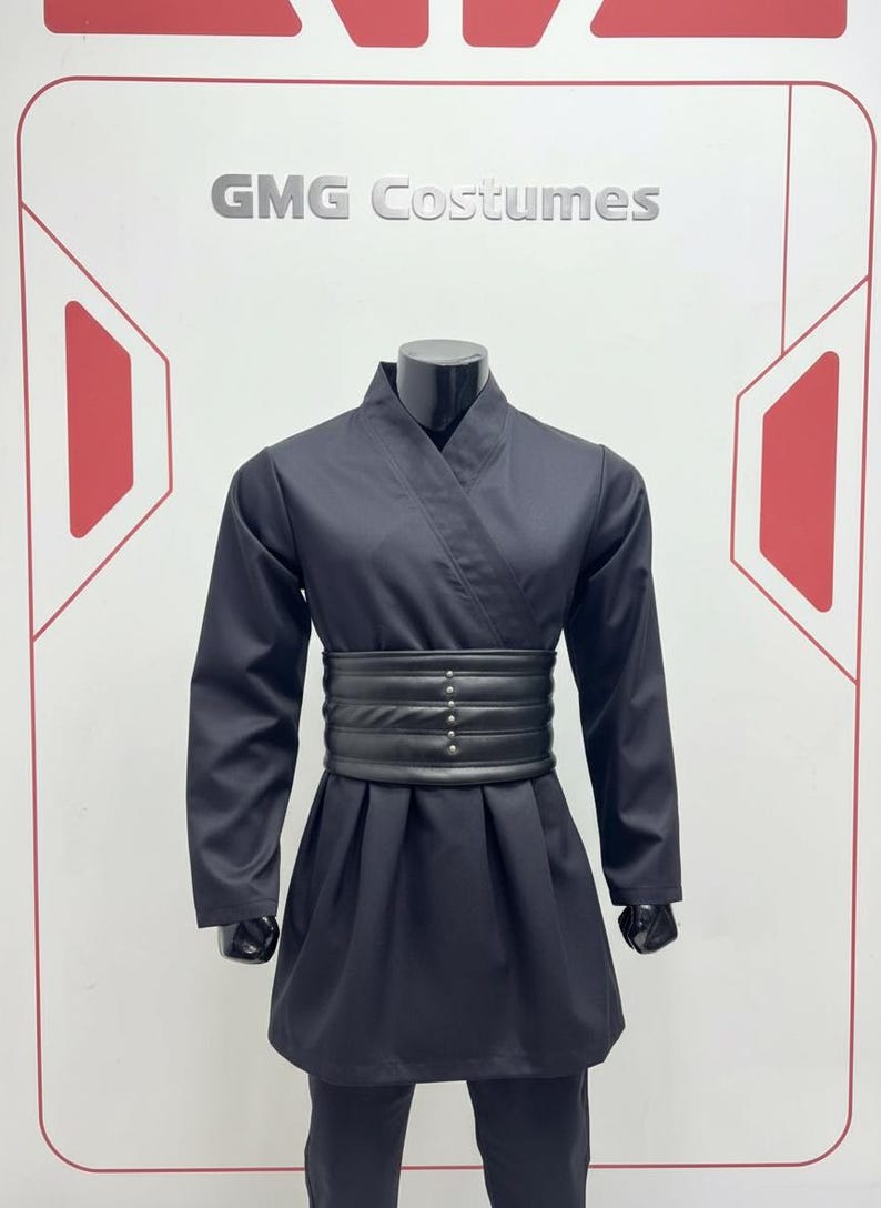 May include: A black costume on a mannequin. The outfit features a wrap-style top, a wide belt with silver studs, and matching trousers. The text "GMG Costumes" is visible. The costume is likely for cosplay or theatrical use, and is a dark colour.