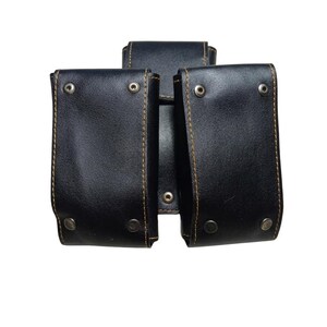 May include: Black leather pouch with three compartments. Each compartment has a flap secured with a metal snap. The edges are stitched with brown thread. The background is white.