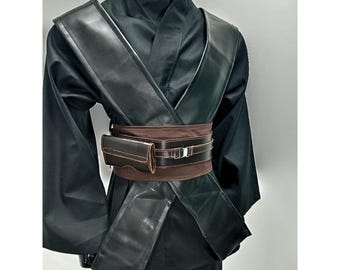 Könnte beinhalten: Schwarzes Kostüm mit einem langärmeligen Oberteil und einer Hose. Das Outfit umfasst einen breiten, dunkelbraunen Gürtel mit passendem Beutel und eine schwarze, lederartige Schärpe über der Brust. Das Kostüm wird auf einer Schaufensterpuppe präsentiert.