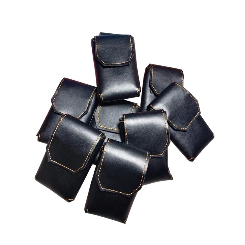 May include: A collection of black leather cases with a flap closure. Each case is rectangular with rounded corners and features contrasting tan stitching. The cases are arranged in a pile against a white background.