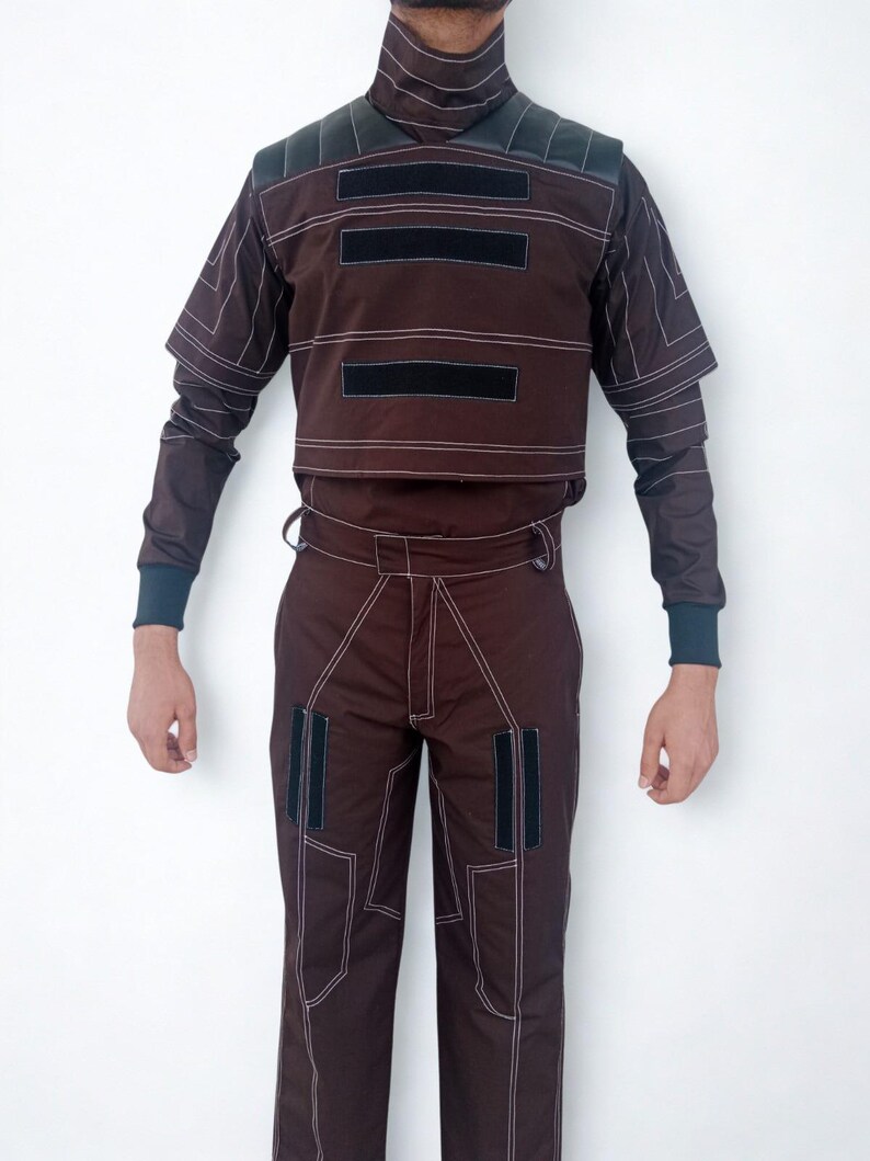 May include: A brown two-piece outfit with white stitching and black accents. The top has a high collar and short sleeves, with three black rectangular patches. The pants have matching white stitching and two black rectangular patches.
