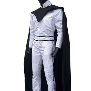 May include: A white jumpsuit with black trim and a matching black cape. The outfit is displayed on a mannequin with a black head. The jumpsuit has a high collar and a black belt. The cape drapes over the shoulders.