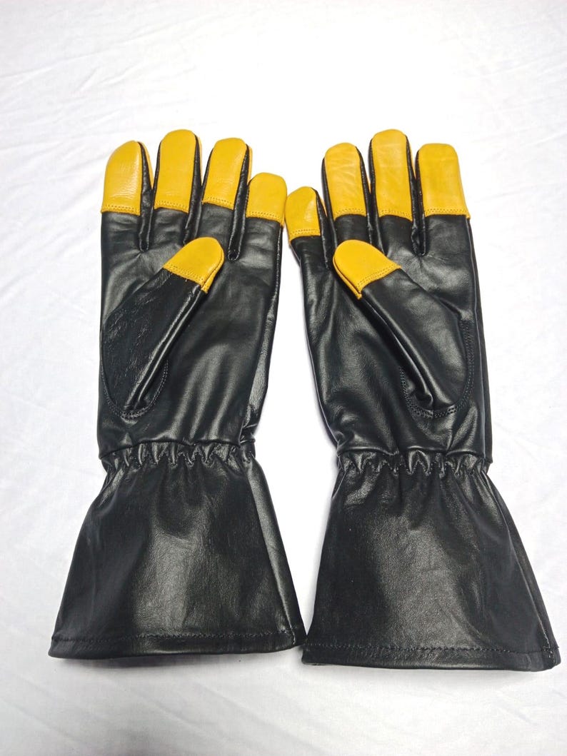 May include: A pair of black leather gloves with yellow fingertips. The gloves have a long cuff and are designed for protection. The gloves are likely for work or outdoor activities.