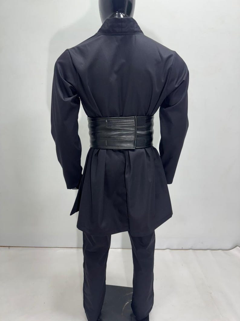 Op de afbeelding: Zwart vechtsportuniform met een brede, zwarte riem. Het uniform bestaat uit een jas met lange mouwen en een bijpassende broek. De riem is gemaakt van een dik, getextureerd materiaal. De outfit wordt gepresenteerd op een mannequin.