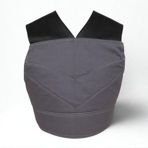 Puede incluir: Un chaleco gris con correas negras para los hombros. El chaleco tiene un dise&ntilde;o de chevr&oacute;n con costuras blancas. El chaleco est&aacute; hecho de una tela duradera y est&aacute; dise&ntilde;ado para usarse sobre la ropa.