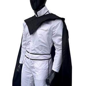 May include: A white jumpsuit with black trim and a matching black cape. The outfit is displayed on a mannequin with a black head and gloves. The jumpsuit has a zip-up front and pockets.