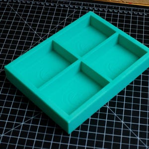 May include: A turquoise blue plastic tray with four compartments. The tray is designed to hold small items, such as jewelry or craft supplies.