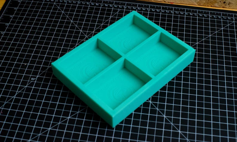 May include: A turquoise blue plastic tray with four compartments. The tray is designed to hold small items, such as jewelry or craft supplies.