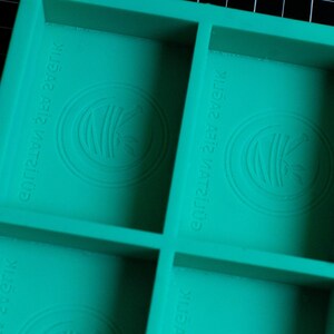 May include: A teal green silicone mold with four square compartments. Each compartment has a raised circular design with the text "Crazy 123 Crazy" embossed on the mold.
