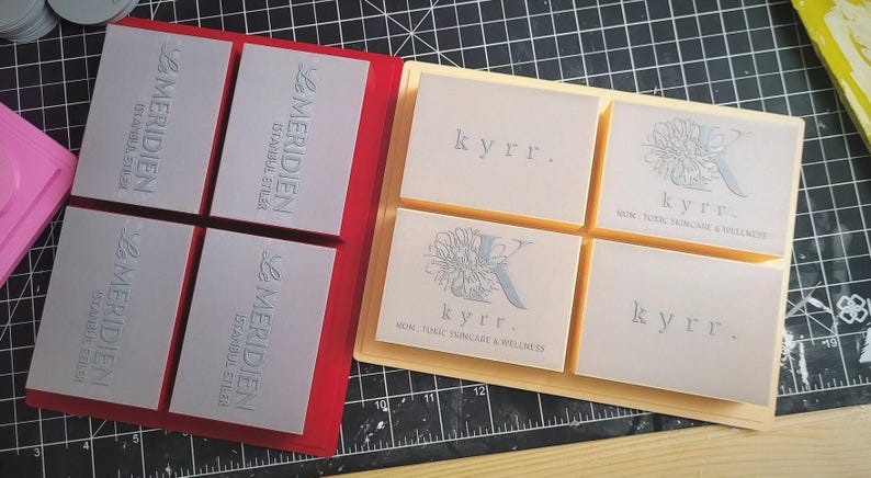 May include: Two sets of silicone molds for making soap bars. The first set is red and has four squares with the text "Le Meridien Istanbul Etles" embossed in silver. The second set is beige and has four squares with the text "kyrr. WOM. FOMC SKINCARE & WELLNESS" embossed in silver.