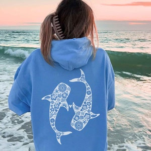 Könnte beinhalten: Ein hellblauer Hoodie mit einem weißen floralen Walhai-Design auf der Rückseite. Der Hoodie hat eine Kapuze mit Kordelzug und eine Kängurutasche.