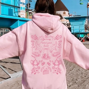 May include: A pink hoodie with a graphic print of a key, birds, teacups, and the text "Protect your heart".