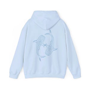 Puede incluir: Una sudadera con capucha azul claro con un gr&aacute;fico de dos tiburones ballena que se miran con un peque&ntilde;o coraz&oacute;n entre ellos.