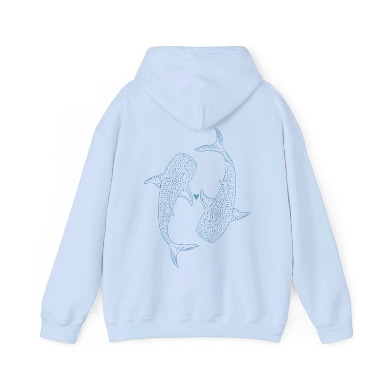 Puede incluir: Una sudadera con capucha azul claro con un gr&aacute;fico de dos tiburones ballena que se miran con un peque&ntilde;o coraz&oacute;n entre ellos.