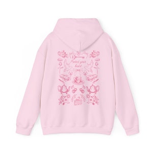 May include: Pink hoodie with a pink graphic print of a key, doves, teacups, cherries, and a cake. The graphic print says "Protect your heart".