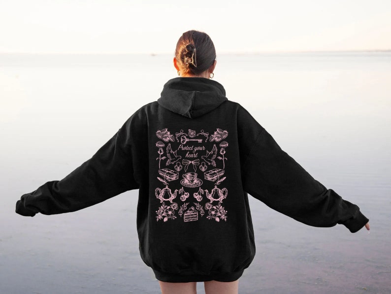 May include: Black hoodie with a pink graphic print on the back. The graphic features a key, a teacup, a cake, and other illustrations. The text "Protect your heart" is included in the graphic.