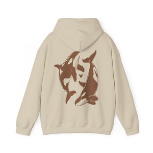 May include: A cream-colored hoodie with a brown graphic of two whales intertwined on the back. The whales are facing each other and have a small heart between them.