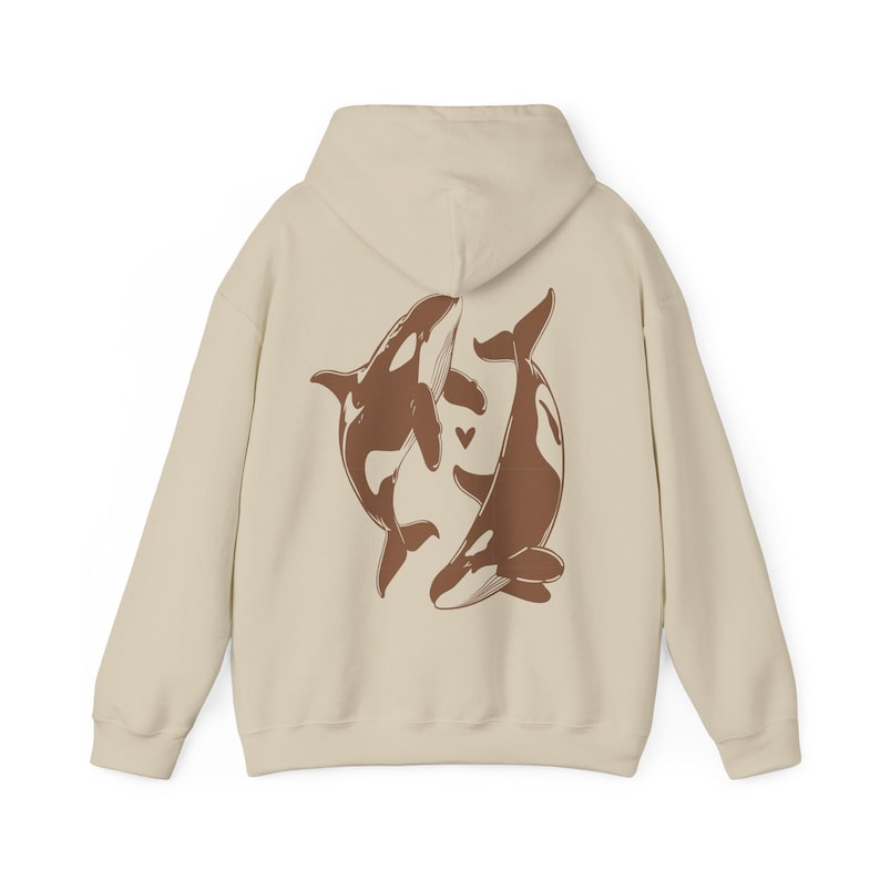 May include: A cream-colored hoodie with a brown graphic of two whales intertwined on the back. The whales are facing each other and have a small heart between them.