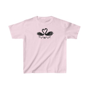 May include: A pink t-shirt with a black silhouette of two swans facing each other with their necks forming a heart shape. The swans are surrounded by a floral design.