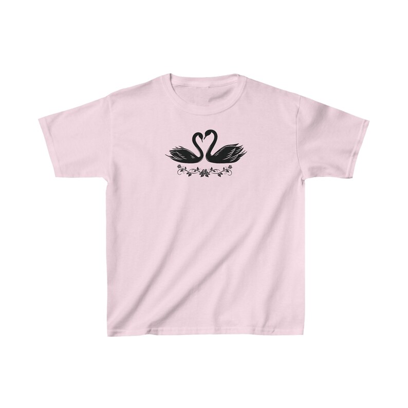 May include: A pink t-shirt with a black silhouette of two swans facing each other with their necks forming a heart shape. The swans are surrounded by a floral design.