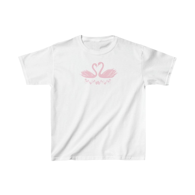 May include: White t-shirt with a pink graphic of two swans facing each other with their necks forming a heart shape. The swans are surrounded by pink floral designs.