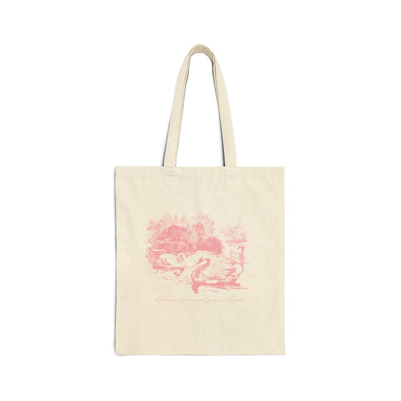 May include: A pink tote bag with a pink illustration of swans on a lake and the text "Kindness is grace and courage is kindness".