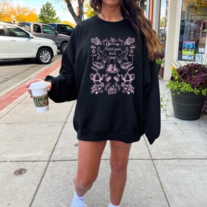 May include: Black sweatshirt with a pink graphic print of various objects, including a key, a heart, a teacup, and flowers. The text "Protect your heart" is printed on the graphic.