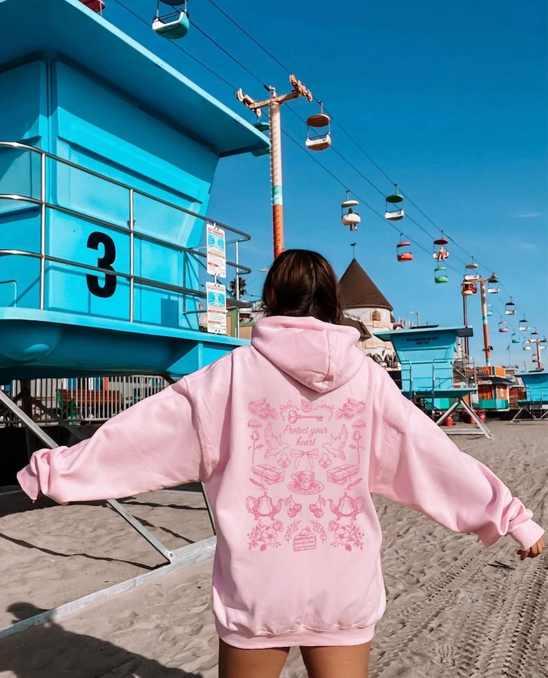 May include: A pink hoodie with a graphic print of a key, birds, teacups, and the text "Protect your heart".