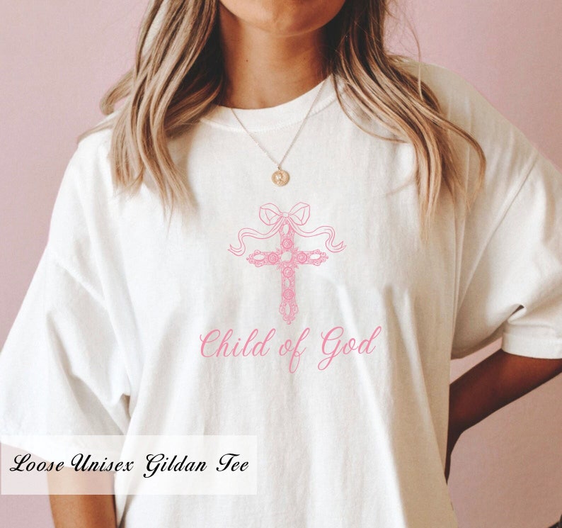 May include: White t-shirt featuring a pink floral cross design and the text "Child of God".