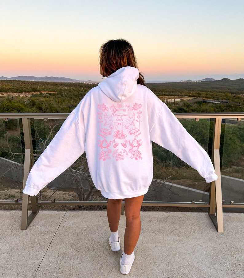 May include: White hoodie with a pink graphic print on the back. The graphic features a variety of images including teacups, flowers, and the text "Painted your heart".