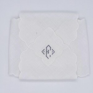 May include: A folded white handkerchief with a scalloped edge. The center features a gray geometric design. The handkerchief is made of a lightweight fabric and is neatly folded, suggesting it is new and unused.
