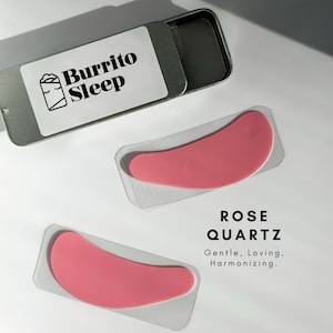 May include: Two pink rose quartz eye masks in clear plastic packaging. The packaging has the text "ROSE QUARTZ" and "Gentle, Loving, Harmonizing."  The eye masks are in a small silver tin with the text "Burrito Sleep" and a cartoon burrito with eyes.
