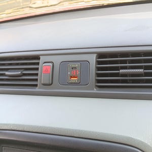 May include: A close-up of a car's dashboard with a black and red emergency button and a digital display showing 13.1V. The display is part of a car charger with a USB port and a Quick Charge logo.