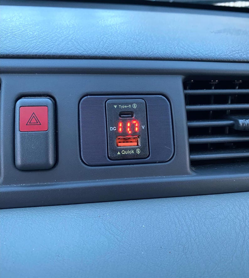 May include: A black car charger with a red digital display showing "11.7" and the text "DC" and "V". The charger has a Type-C port and a Quick Charge port.