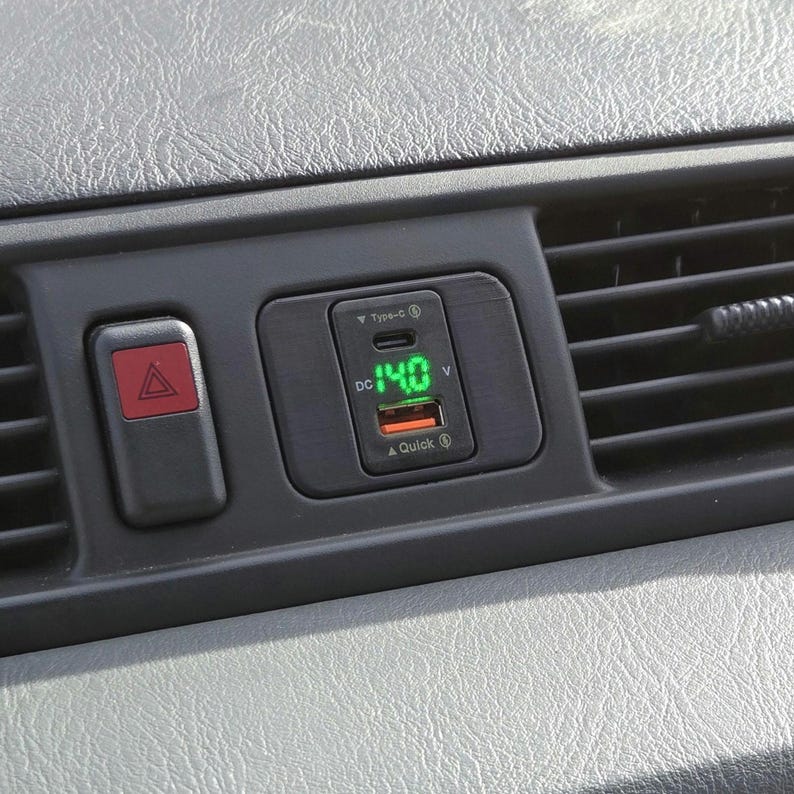 May include: A black car charger with a green digital display showing "14.0 V". The charger has a USB-C port and a Quick Charge logo.