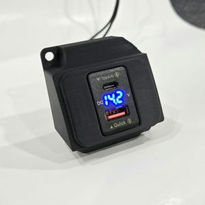 May include: A black car charger with a USB-C and USB-A port. The charger has a digital display that shows "DC 14.2 V".