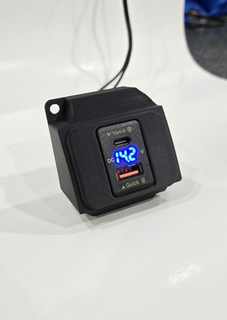 May include: A black car charger with a USB-C and USB-A port. The charger has a digital display that shows "DC 14.2 V".