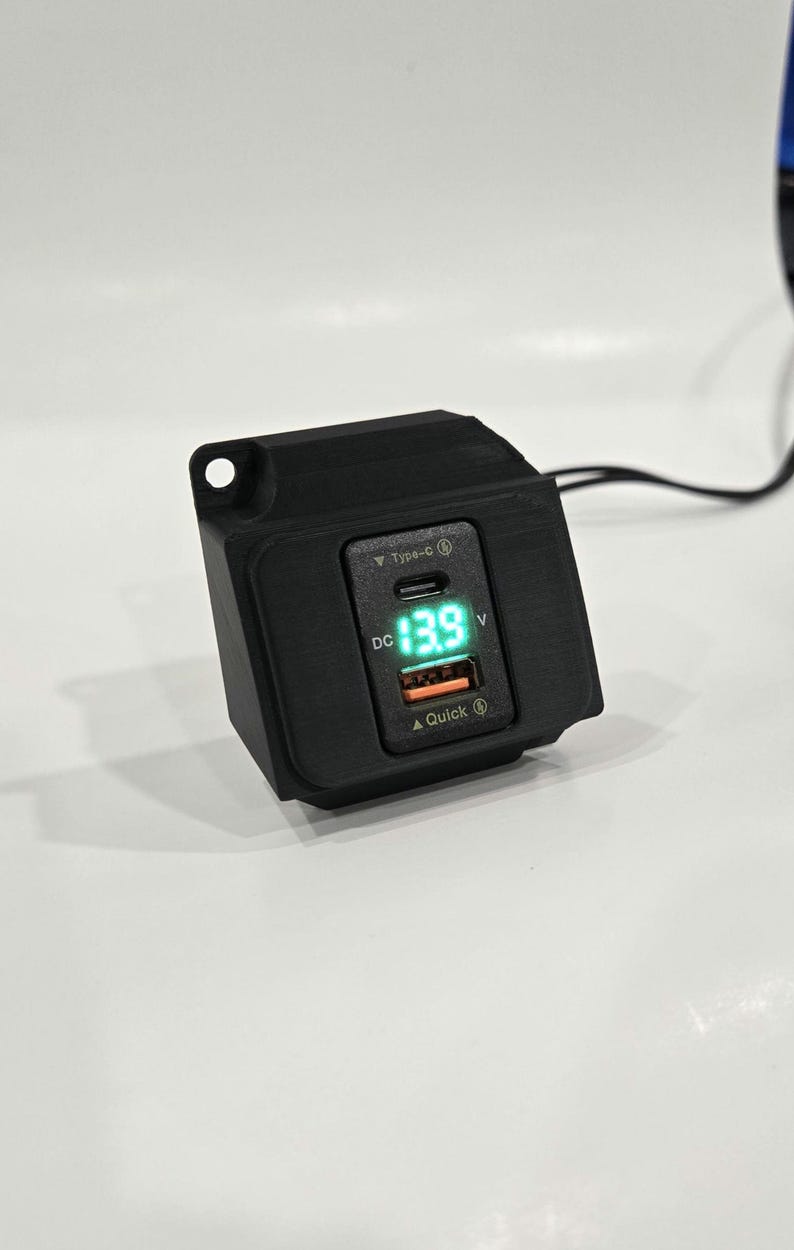 May include: Black car charger with a digital display showing 13.9 volts. The charger has a USB-C port and a Quick Charge port.