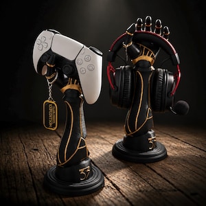 Könnte beinhalten: Zwei schwarz-goldene handförmige Ständer auf runden Sockeln mit der Nummer 37. Ein Ständer hält einen weißen Gamecontroller mit einer Erkennungsmarke mit der Aufschrift CLAIR OBSCUR EXPEDITION, der andere schwarze und rote Gaming-Kopfhörer.