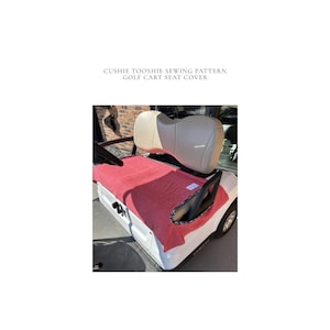 May include: A white golf cart with a red seat cover. The seat cover is draped over the seat and has a black and white patterned trim. The text "CUSHIE TOOSHIE SEWING PATTERN GOLF CART SEAT COVER" is at the top.