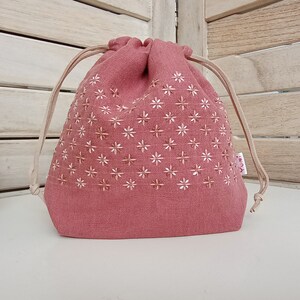 May include: A pink drawstring bag with a white floral pattern and a small pink label that says "Yumi".