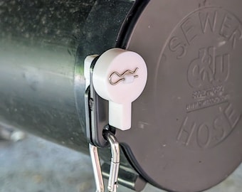 May include: A white plastic sewer hose connector with a silver clip and a silver safety pin. The connector is attached to a gray sewer hose.