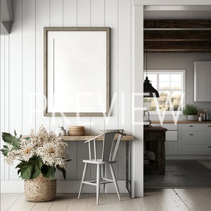 Könnte beinhalten: Ein weißes Esszimmer im Landhausstil mit einem Holztisch und einem weißen Stuhl. Ein großes gerahmtes Bild hängt an der Wand hinter dem Tisch. Ein Strauß weißer Blumen in einem geflochtenen Korb steht auf dem Tisch. Der Raum hat weiße Wände und Holzböden.