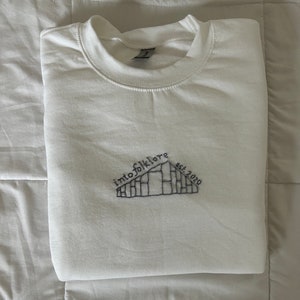 May include: White sweatshirt with a black embroidered design that says "into folklore est. 2020".