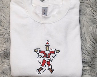 May include: White crewneck sweatshirt with an embroidered Santa Claus design. The Santa Claus is depicted with arms outstretched, wrapped in Christmas lights, and wearing a red suit and hat.