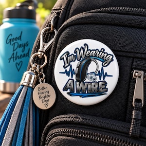 May include: A round white pinback button featuring a black hearing aid illustration, a blue heartbeat line, and the text I'm Wearing A Wire. Attached is a silver keychain with a round charm engraved with Better Hearing Brighter Days and a heart.