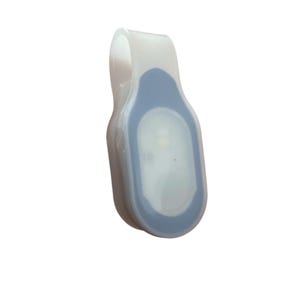 May include: A white and blue LED safety light with a clip. The light has a rounded rectangular shape with a blue center and a clear, curved clip. The light is designed to be attached to clothing or gear for visibility.