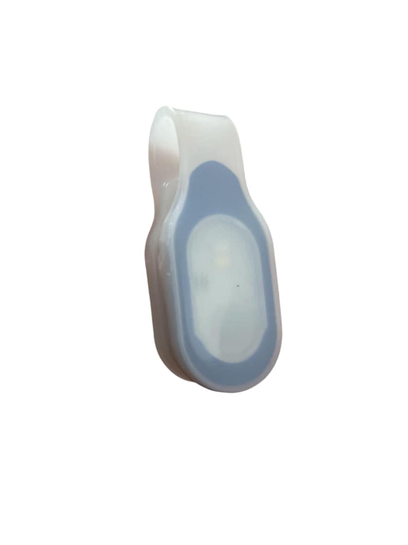 May include: A white and blue LED safety light with a clip. The light has a rounded rectangular shape with a blue center and a clear, curved clip. The light is designed to be attached to clothing or gear for visibility.