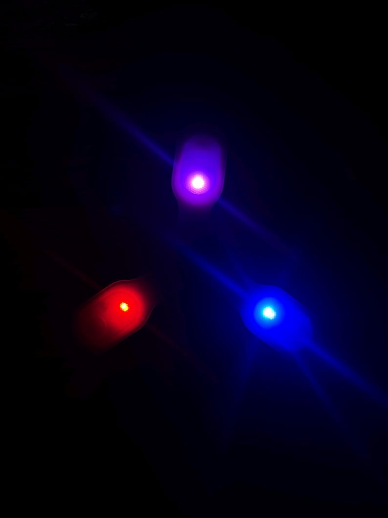 May include: Three glowing LED lights in red, blue, and purple against a black background. The lights are oval-shaped and emit a bright, diffused glow. The image has a dark, space-like aesthetic.