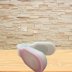 May include: Two white and pink massage tools are displayed on a wooden surface. The tools have a curved design with a rounded end. The background features a light brown brick wall.
